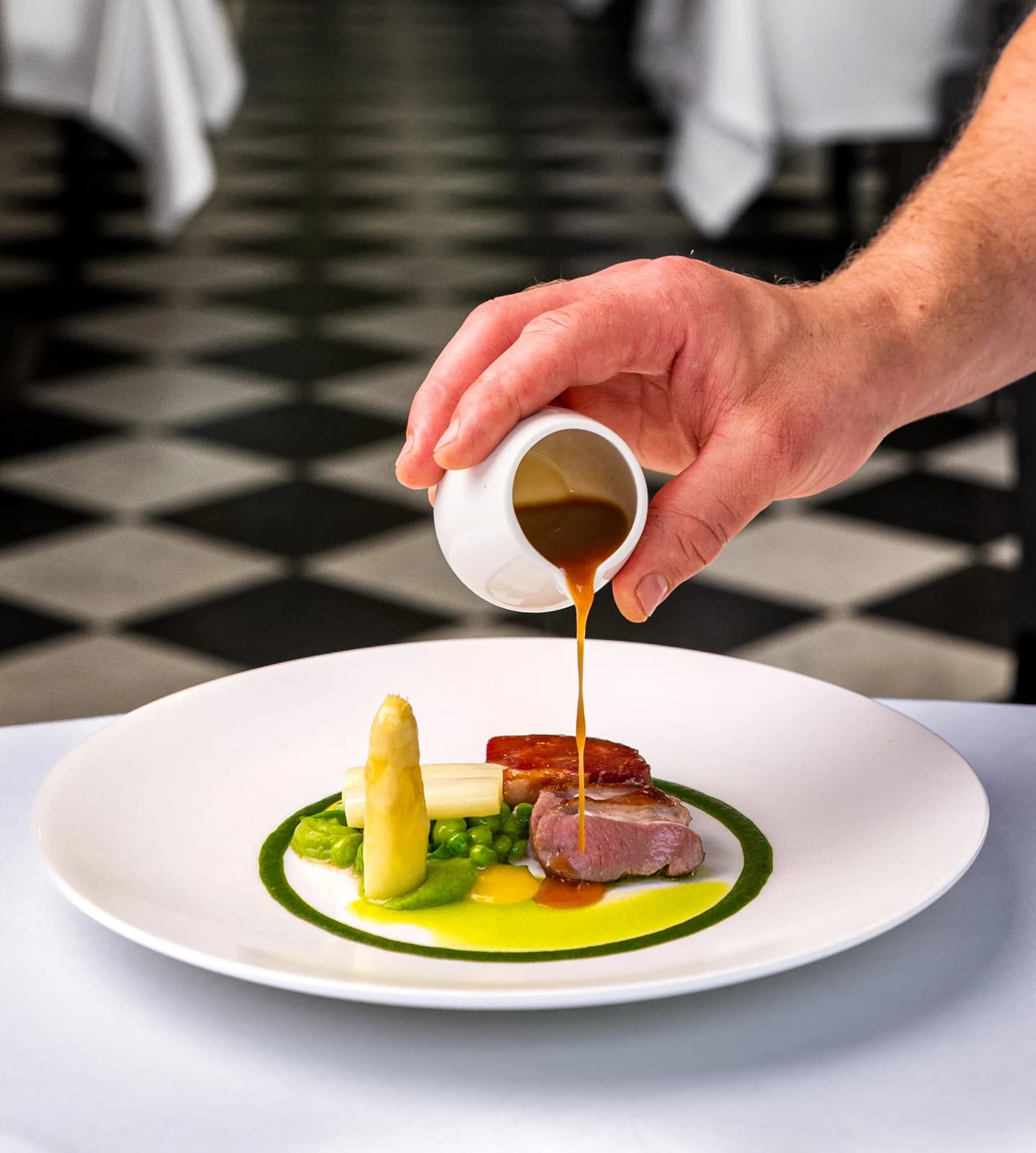 Een hand schenkt saus uit een wit kannetje over een zorgvuldig opgemaakt gerecht bij Landgoed Groenendaal.
