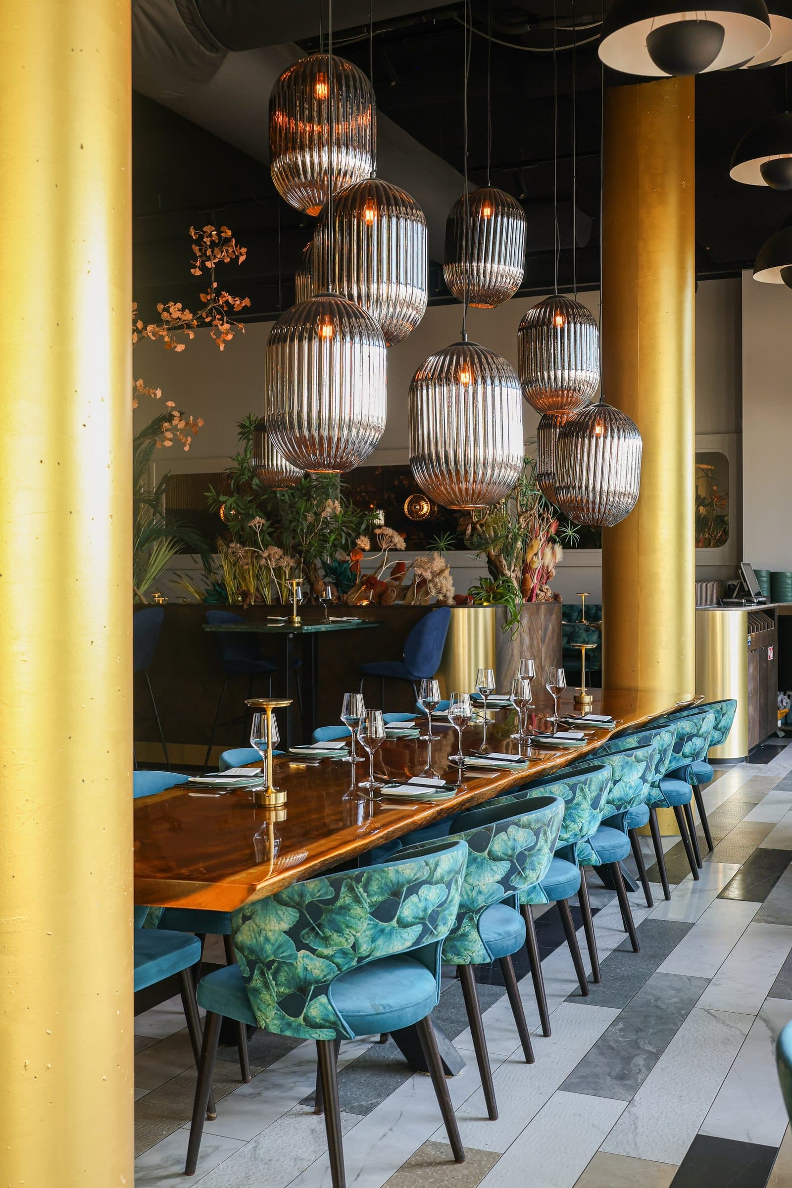 Lange tafel gedekt voor het diner bij ChouChou, blauwe stoelen onder een cluster glazen hanglampen.