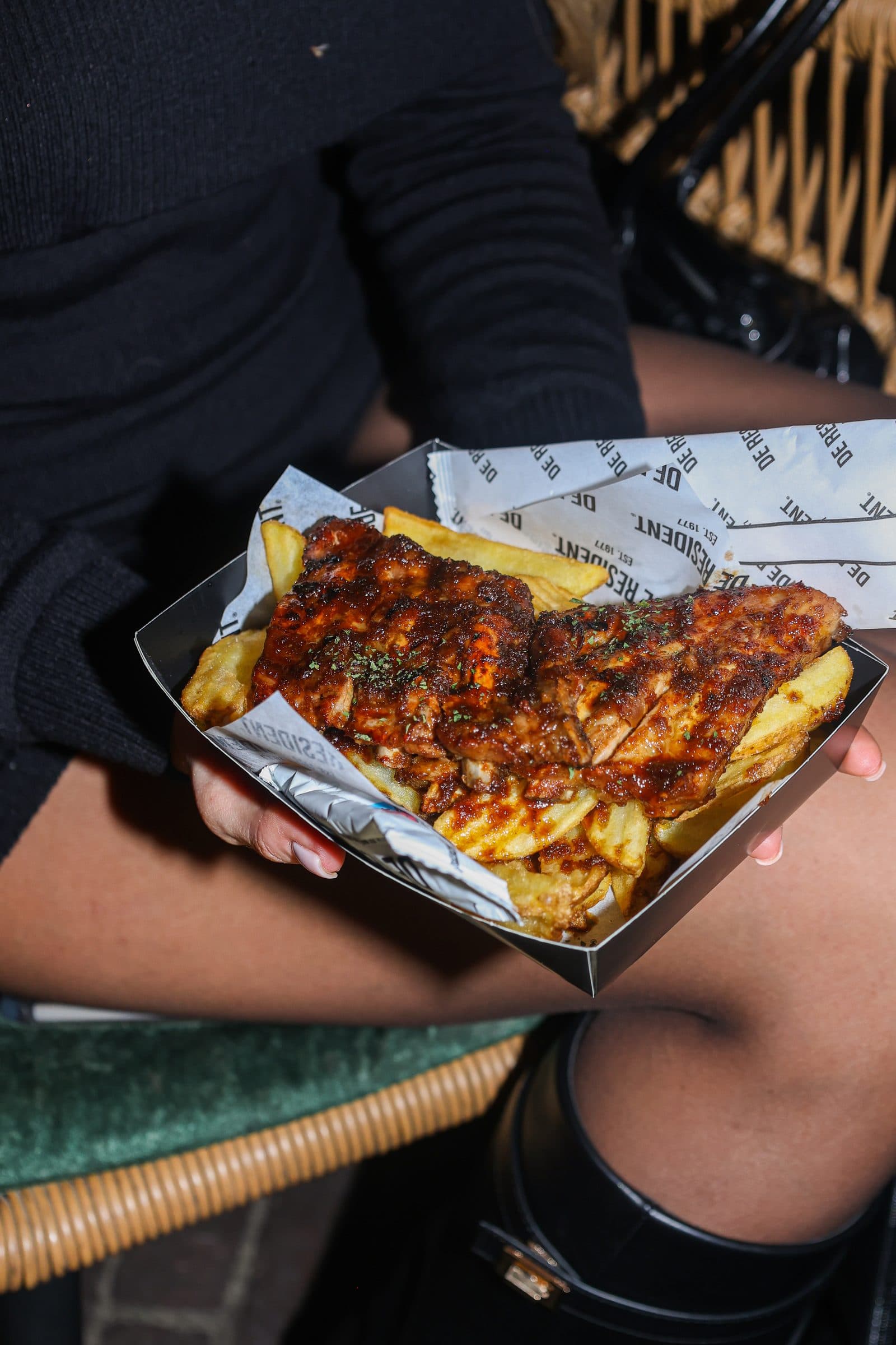 Een gast houdt een mandje met friet en een gegarneerd gerecht vast bij Foodhall Scheveningen.