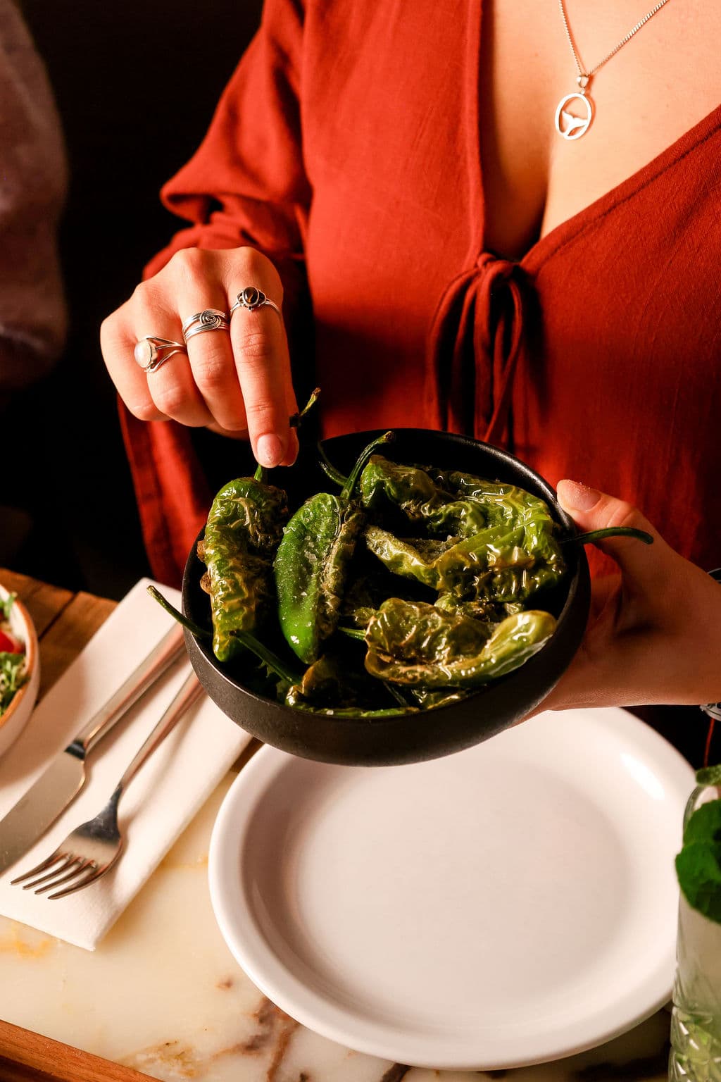 Een gast in rood houdt een kom met geblakerde groene pepers vast bij Lavash.