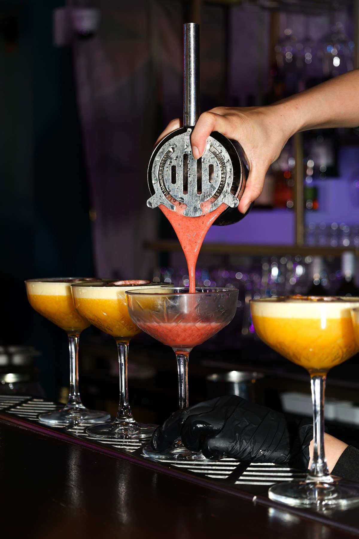Een rode cocktail wordt tussen goudgele cocktails ingeschonken achter de bar bij Madam Chen in Rotterdam.