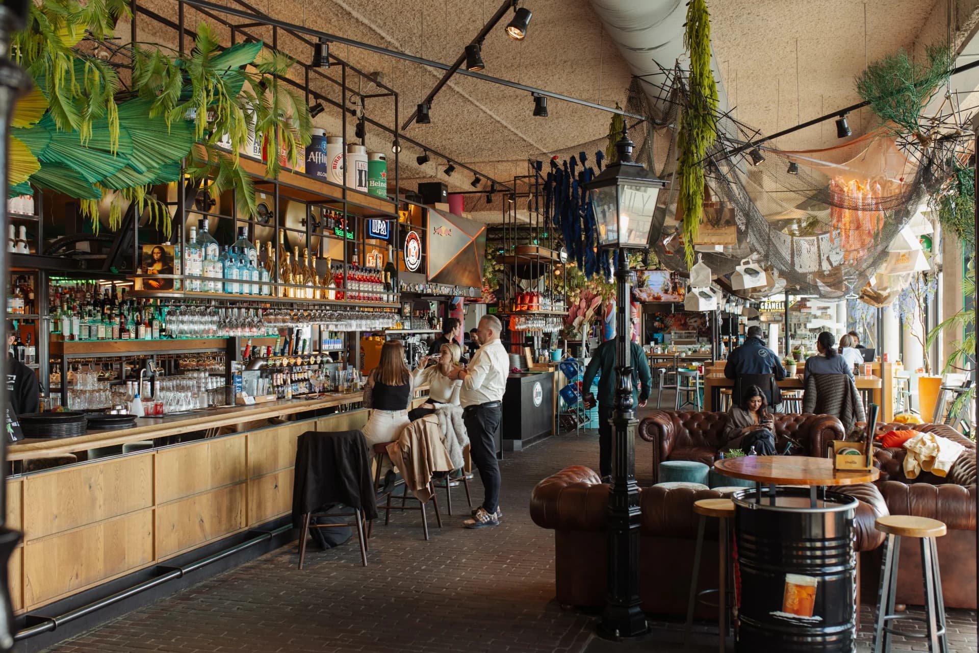 Warm verlicht interieur met een lange bar, planten en zitplekken bij Foodhall Scheveningen.