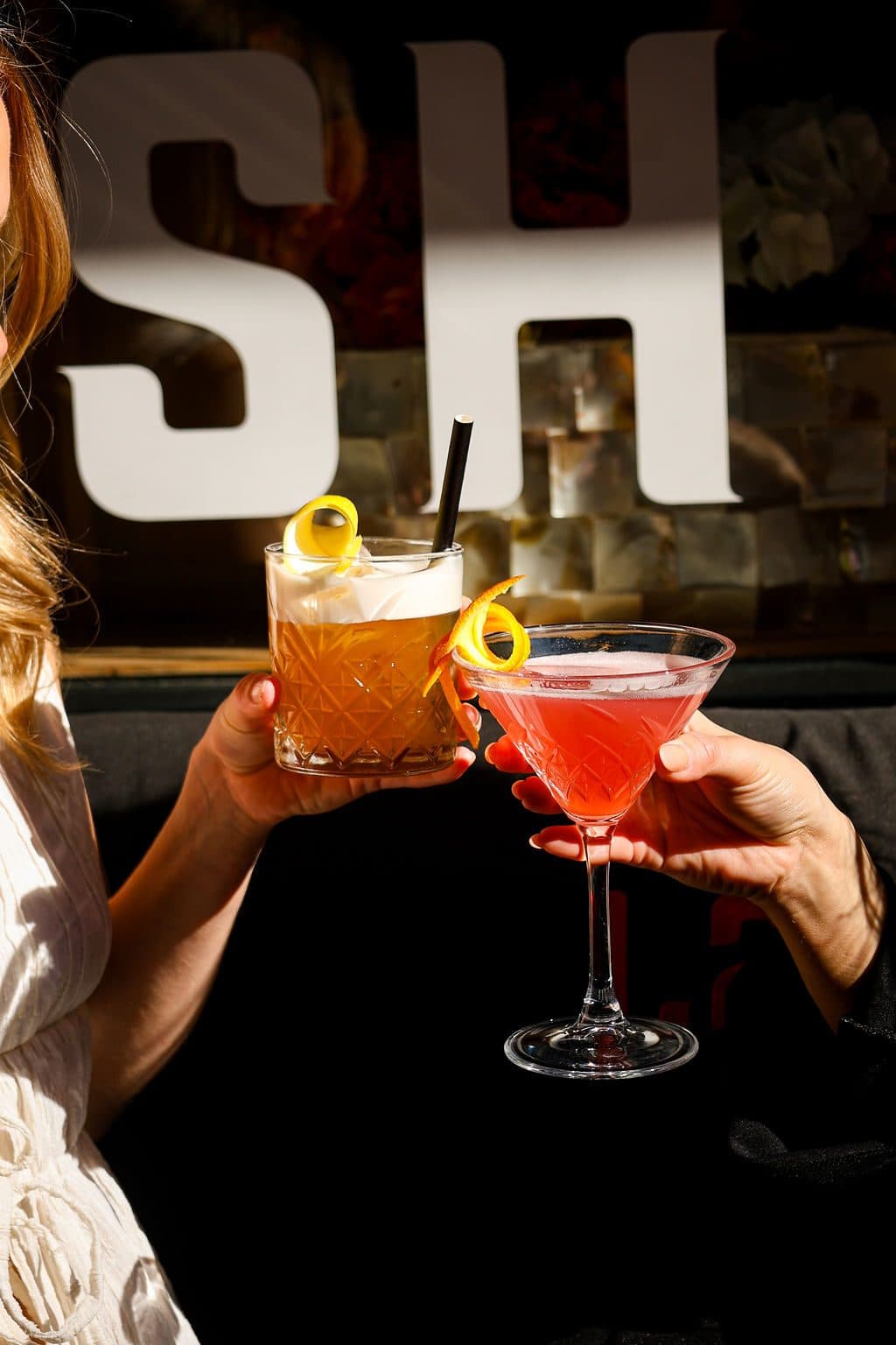 Twee gasten proosten met cocktails voor de verlichte letters bij Lavash.